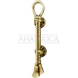 May include: A decorative brass door pull with a rope design. The pull features a loop at the top, a knotted center, and a tassel at the bottom. The pull is mounted on two circular plates with a starburst pattern. The word "ANATOLICA" is printed on the pull.