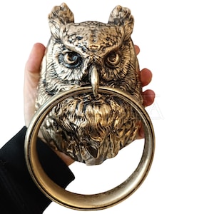 May include: A gold owl door knocker with a ring handle. The owl's eyes are black and the details are intricate.