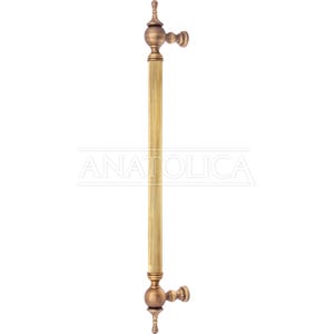 May include: A gold-toned door pull handle with a fluted design and rounded ends. The handle is mounted on a wall.
