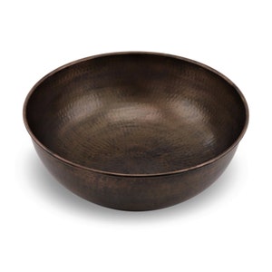 May include: A large, round, hammered copper bowl with a dark brown patina. The bowl is empty and has a slightly textured surface.