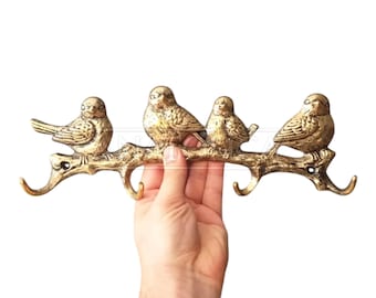 May include: Gold metal bird hook rack with three birds perched on a branch. The rack has three hooks for hanging keys, coats, or other items.