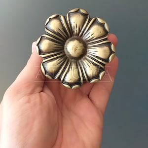 May include: A gold-toned metal flower-shaped decorative piece with a raised center and intricate details.