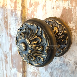 Peut inclure: Une paire de boutons de porte ornés avec une finition noire et dorée. Les boutons présentent un motif floral détaillé.