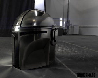 May include: A black and silver Mandalorian helmet with a visor. The helmet is made of metal and has a textured surface.