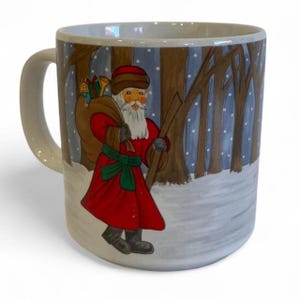 May include: A ceramic mug featuring a festive Santa Claus design. Santa is depicted in a red coat, carrying a sack of gifts and a walking stick, set against a snowy forest backdrop. The mug has a white handle and a light-colored rim.
