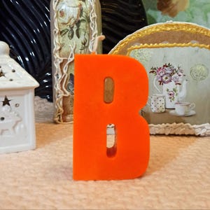Front view of a large orange letter B candle.
