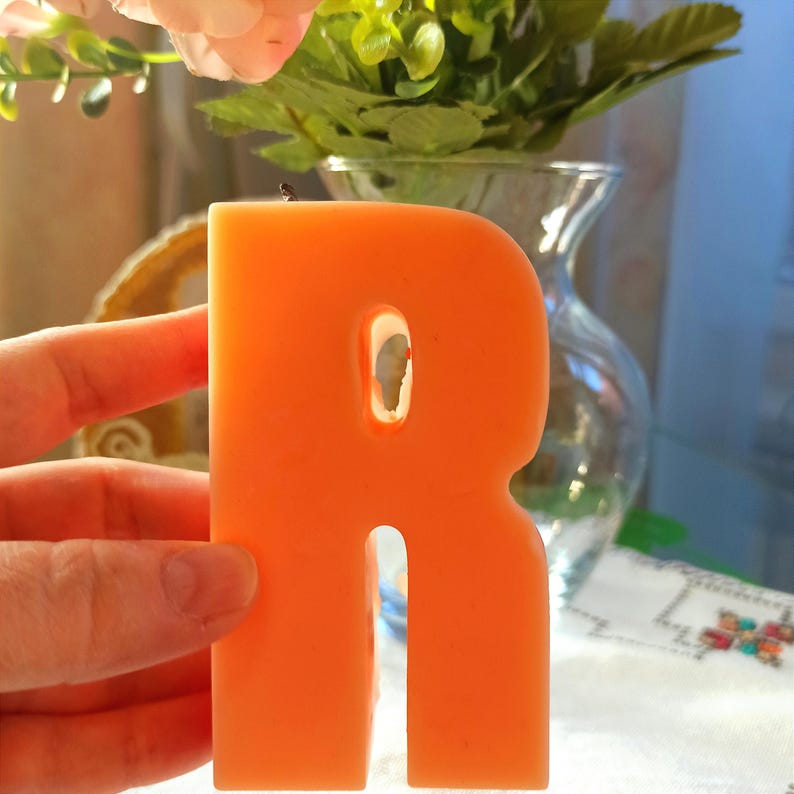 Large orange letter R candle held in hand for size reference.