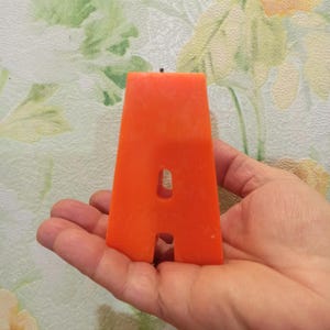 Large orange letter A candle held in hand for size reference.