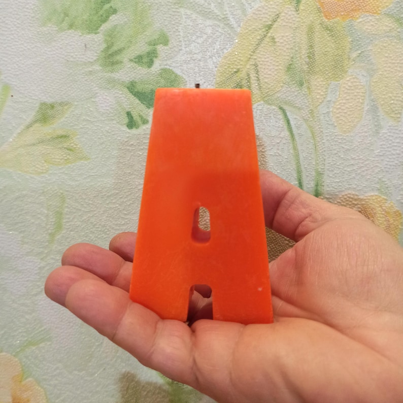 Large orange letter A candle held in hand for size reference.