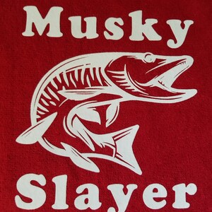 以下が含まれることがあります： 赤い生地に「Musky Slayer」という白い文字と、魚の白いシルエットが描かれている。