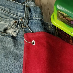 以下が含まれることがあります： 青いジーンズに金属製のフックが付いた赤いタオル。フックには銀色のリングが付いています。