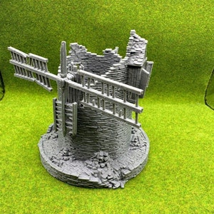 May include: A gray, stone-like miniature windmill with a broken roof and a single blade. The windmill is set on a base of rubble and is surrounded by green grass.