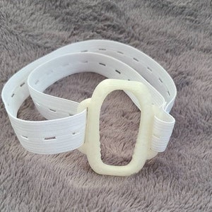 May include: White elastic band with a white plastic buckle. The buckle has a rectangular shape with a rounded oval opening.