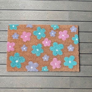 May include: A brown coir doormat with a floral pattern. The flowers are in shades of pink, blue, and purple.