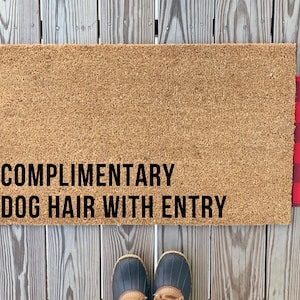以下が含まれることがあります： 「COMPLIMENTARY DOG HAIR WITH ENTRY」の黒い文字が入った、天然コイア繊維製の長方形のドアマット。マットの両側に赤と黒のバッファローチェックのアクセントがあります。下には青と茶色のブーツのペアがあります。