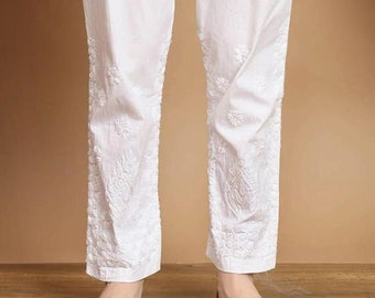 May include: White trousers featuring an elasticized waistband with a drawstring closure and side pockets. The lower portion of the pant legs displays intricate white tonal embroidery with floral patterns, ending in a straight hemline.