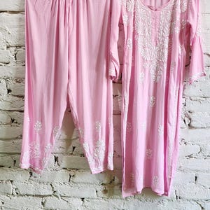 Puede incluir: Un conjunto de dos piezas de color rosa claro que consta de una t&uacute;nica de manga larga y pantalones a juego. La t&uacute;nica presenta un cuello redondo y bordados florales blancos en el pecho y las mangas. Los pantalones tienen una cintura fruncida.