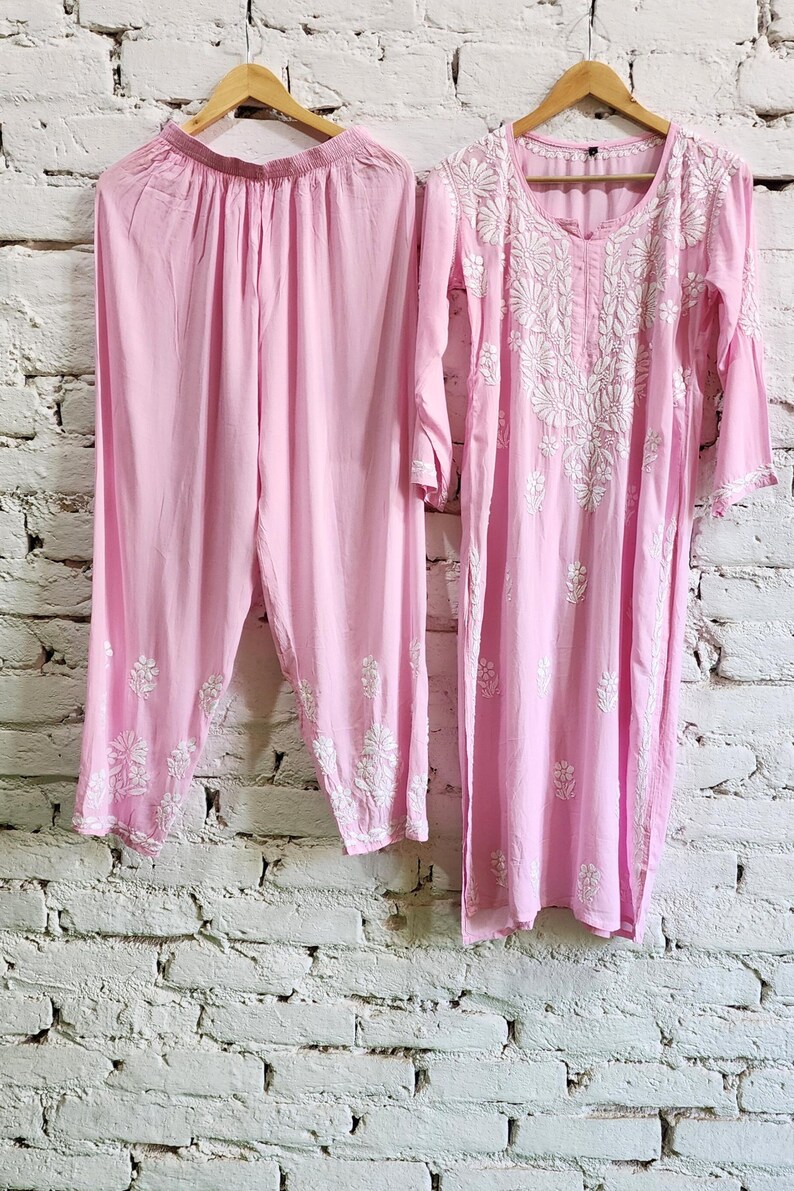 Puede incluir: Un conjunto de dos piezas de color rosa claro que consta de una t&uacute;nica de manga larga y pantalones a juego. La t&uacute;nica presenta un cuello redondo y bordados florales blancos en el pecho y las mangas. Los pantalones tienen una cintura fruncida.