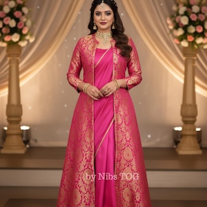 May include: A woman wearing a vibrant pink sari with a matching long jacket. The jacket features a gold brocade pattern. The outfit is accessorized with gold jewelry, including a necklace, earrings, and bracelets. The text "by Nibs TOG" is visible on the garment.