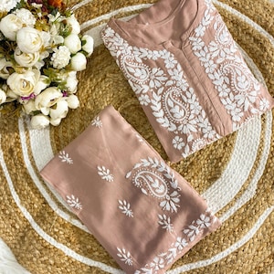 Op de afbeelding: Een tweedelige set in oudroze kleur, bestaande uit een tuniek met lange mouwen en een bijpassende broek. Beide kledingstukken zijn versierd met gedetailleerd wit borduurwerk in bloem- en paisley-motieven. De tuniek heeft een split-halslijn.
