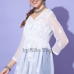 May include: White sheer top with embroidered details and a tie at the waist. The top has a V-neckline and 3/4 sleeves. The text "by Nibs Tog" is visible on the front of the top.