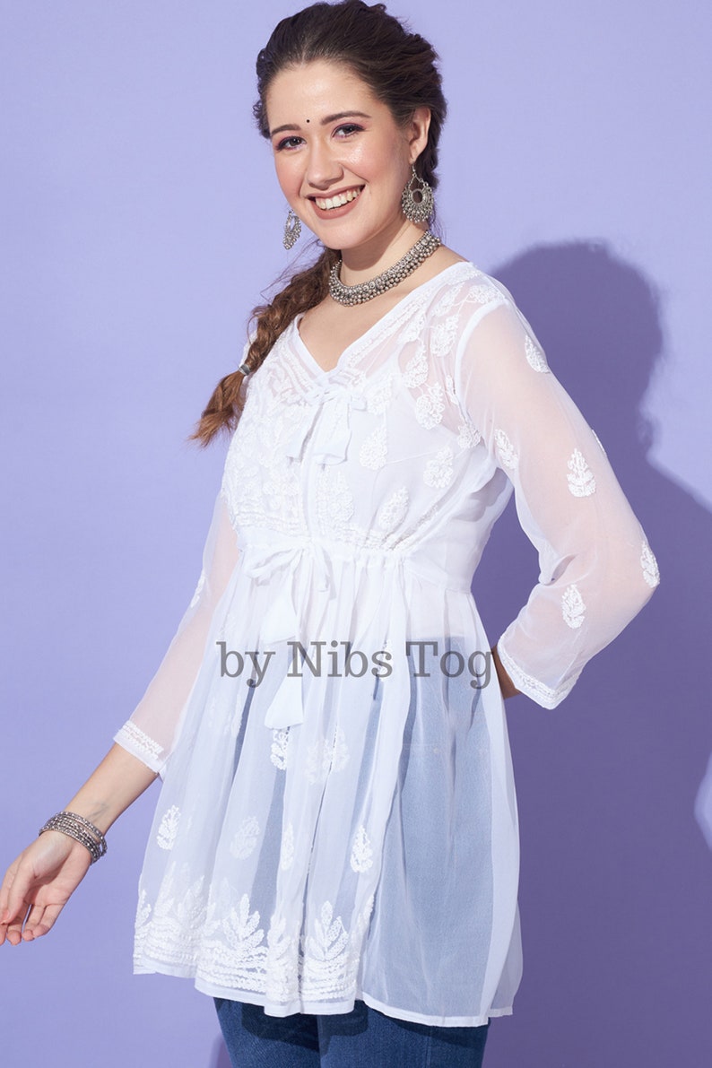 May include: White sheer top with embroidered details and a tie at the waist. The top has a V-neckline and 3/4 sleeves. The text "by Nibs Tog" is visible on the front of the top.