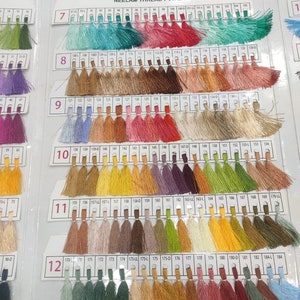 May include: A color chart of thread samples, numbered 7 through 12, with each number representing a different color category. The chart is organized in rows of 20 thread samples, with each sample having a small tassel at the end. The thread colors range from light to dark, and include shades of blue, green, pink, red, brown, yellow, and orange.