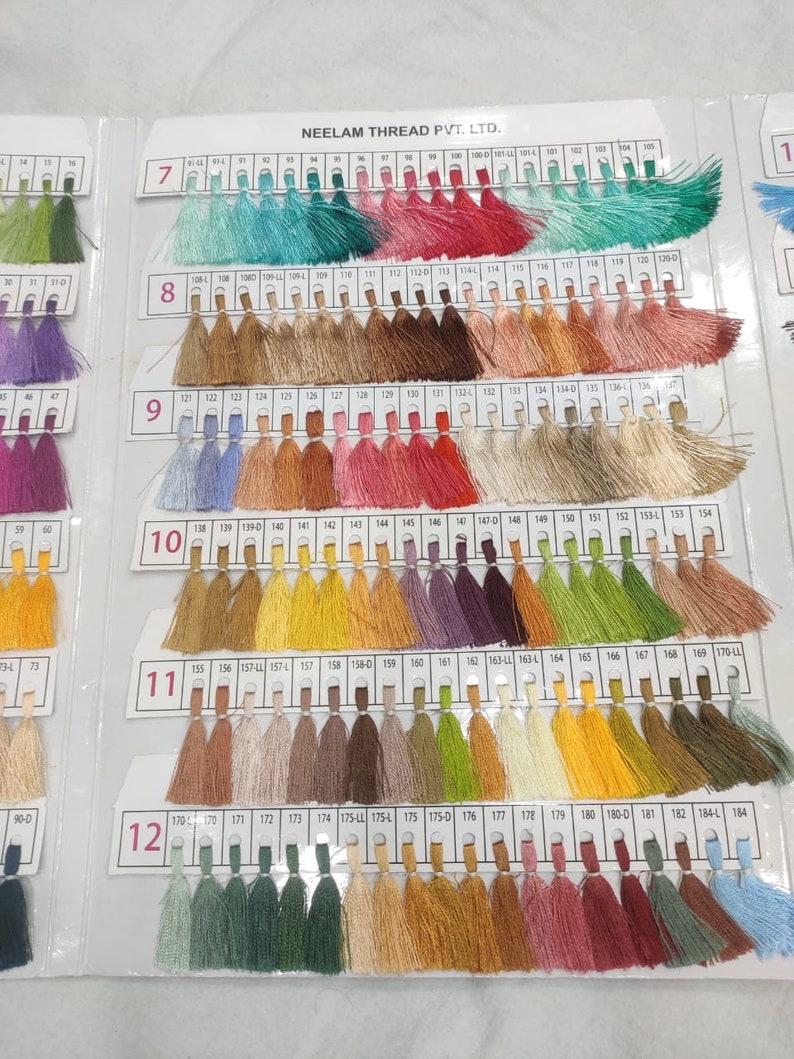 May include: A color chart of thread samples, numbered 7 through 12, with each number representing a different color category. The chart is organized in rows of 20 thread samples, with each sample having a small tassel at the end. The thread colors range from light to dark, and include shades of blue, green, pink, red, brown, yellow, and orange.
