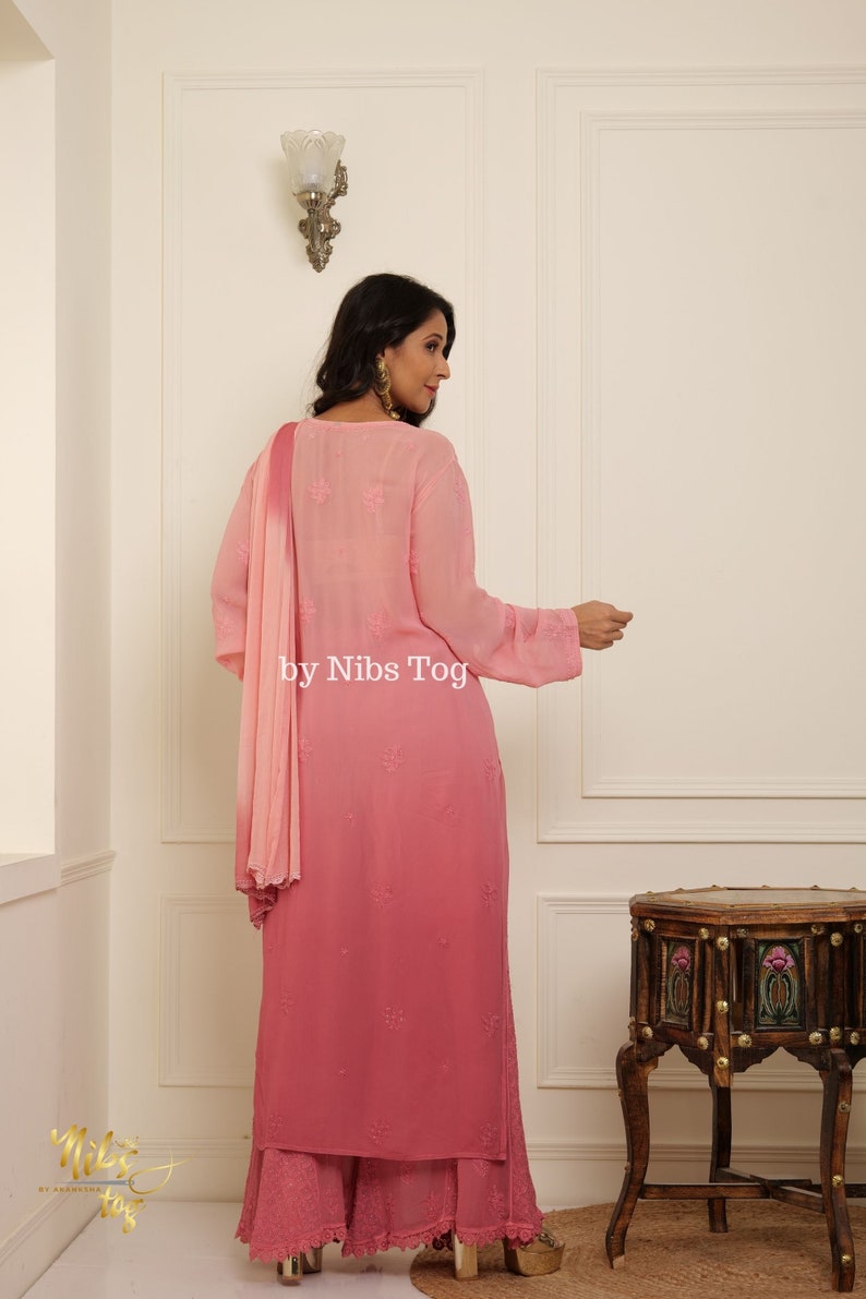 May include: A pink ombre kurta with embroidered details and a matching palazzo pant. The kurta has a round neckline and three-quarter sleeves. The palazzo pant has a lace trim at the bottom. The outfit is paired with a pink chiffon dupatta.