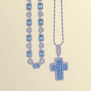 May include: Two pieces of jewelry: a necklace with a cross pendant and a bracelet. Both are silver-toned and feature blue and clear rectangular and round-cut stones. The cross pendant is encrusted with blue stones.