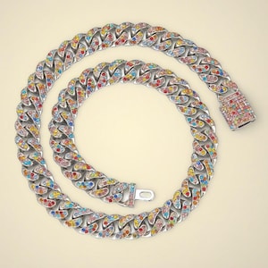 Puede incluir: Un collar de cadena plateada con un diseño colorido y adornado con gemas. El collar presenta una gruesa cadena de eslabones, con cada eslabón adornado con una variedad de gemas de colores. El cierre también está adornado con gemas.