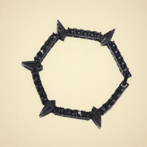Puede incluir: Una pulsera negra con un diseño geométrico. La pulsera presenta una serie de piedras negras de corte cuadrado y puntas triangulares. Las puntas están espaciadas uniformemente alrededor de la pulsera. La pulsera está hecha de un material oscuro y brillante.
