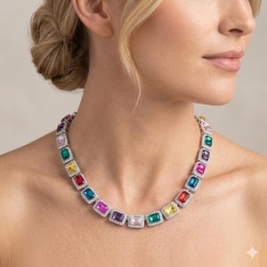 May include: A silver-toned necklace featuring a series of rectangular, multi-colored gemstones in shades of red, blue, green, yellow, purple, and pink. Each large central stone is surrounded by a border of small, clear, sparkling pavé crystals.