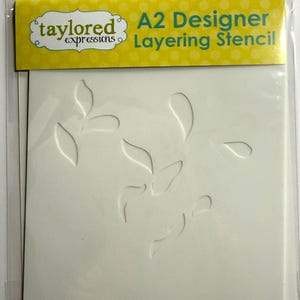 May include: A2 Designer Layering Stencil by Taylored Expressions. The stencil is white with a leaf design. The packaging is clear plastic with a yellow header that has the brand name and product description.
