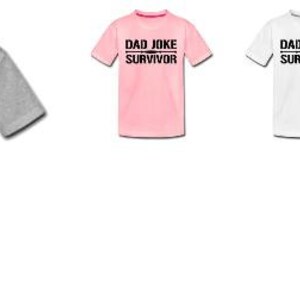 Pu&ograve; includere: Una collezione di magliette a maniche corte in vari colori: grigio, rosa, bianco e giallo. Ogni maglietta presenta la scritta nera "DAD JOKE SURVIVOR" centrata sul davanti. Le magliette sono esposte su sfondo bianco.