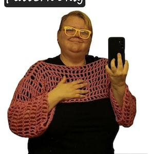 Puede incluir: Un top de crochet con mangas largas de color rosa. El top tiene un diseño suelto y de tejido abierto.