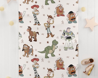 Puede incluir: Un fondo blanco con un patrón repetido de personajes de Toy Story, incluyendo Woody, Buzz Lightyear, Jessie, Rex y el Sr. y la Sra. Potato Head. Los personajes están rodeados de estrellas marrones.