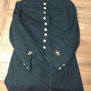May include: A dark navy blue military-style tunic featuring a high collar with gold embroidery, gold-toned buttons down the front, shoulder epaulets with red and gold trim, and embroidered crown insignias on each sleeve cuff.