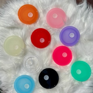 May include: Assortment of ten round, colorful plastic lids with a small hole in the center. The lids are in various colors, including orange, pink, red, purple, clear, pink, green, black, and light blue.