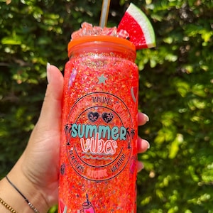 Puede incluir: Un vaso naranja brillante lleno de purpurina con la frase "Summer Vibes". Tiene una pajita y una rodaja de sandía encima. El diseño incluye palmeras, gafas de sol y las palabras "Beach Days, Sunshine, Vacation".