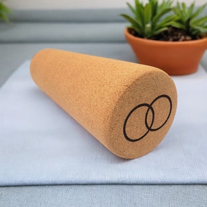 Può includere: Un rullo di sughero marrone con un designo nero di due cerchi intrecciati. Il rullo è su una superficie di tessuto blu chiaro.