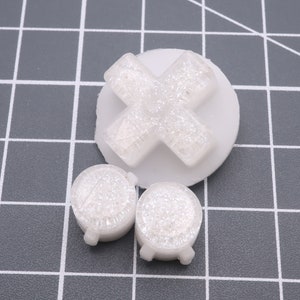 May include: Three white plastic buttons with a sparkly finish. One button is shaped like a cross and the other two are round.