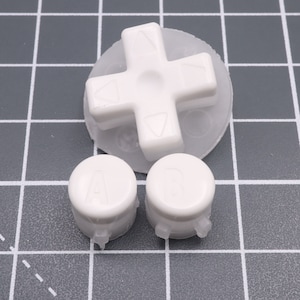 Pode incluir: Botões de substituição brancos para um controlador de console de jogos. O conjunto inclui um direcional, um botão A e um botão B.
