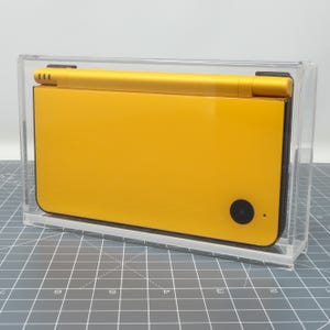 May include: A yellow Nintendo DS handheld gaming console in a clear plastic display case.