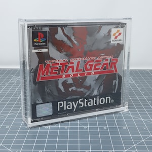 Peut inclure: Une boîte en plastique transparente contenant une cartouche de jeu PlayStation pour Metal Gear Solid. La boîte de jeu est noire avec du texte rouge et blanc. Le jeu est classé PAL et est un jeu d'action d'espionnage tactique.