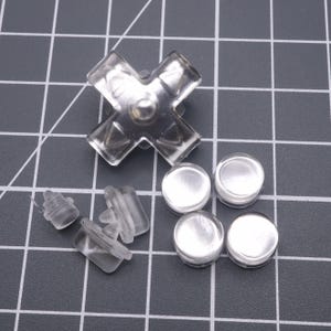 以下が含まれることがあります： ビデオゲームコントローラー用の透明なプラスチック製交換ボタンのセット。セットには、4方向の十字キーと丸いボタンが4つ含まれています。