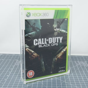 May include: A clear plastic case containing a video game. The game is Call of Duty: Black Ops for the Xbox 360. The game cover features a soldier holding a gun and the game title in white text on a black background. The game is rated 18+.