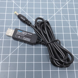 以下が含まれることがあります： 黒いUSBケーブルと、黒い箱に「SEGA GAME GEAR USB CABLE」と「INPUT: 5V 2A MAX OUTPUT: 9V 0.7」と書いてあり、白黒のロゴに「JELLYbELLY CUSTOMs」と書いてある。