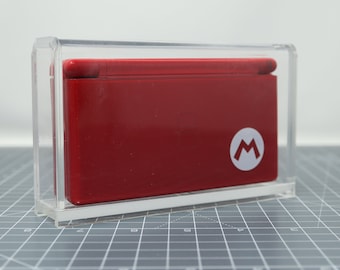 May include: A red Nintendo DS game console in a clear plastic display case. The console has a white "M" logo on the front.