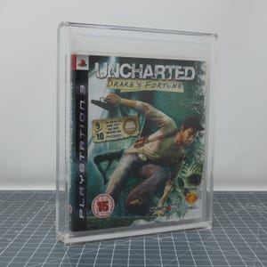 May include: A video game case for "Uncharted: Drake's Fortune" for PlayStation 3, encased in a clear protective case. The cover art features a man with a gun, set against a jungle backdrop. The game is rated "15".